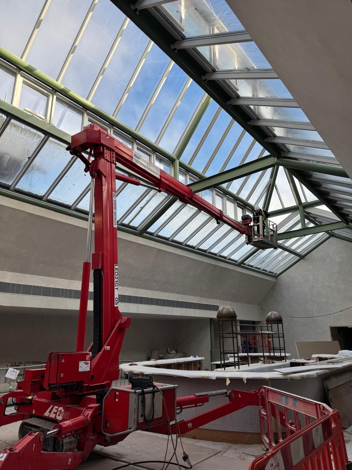 Red spider lift working indoors beneath a glazed roof with an operator in the basket