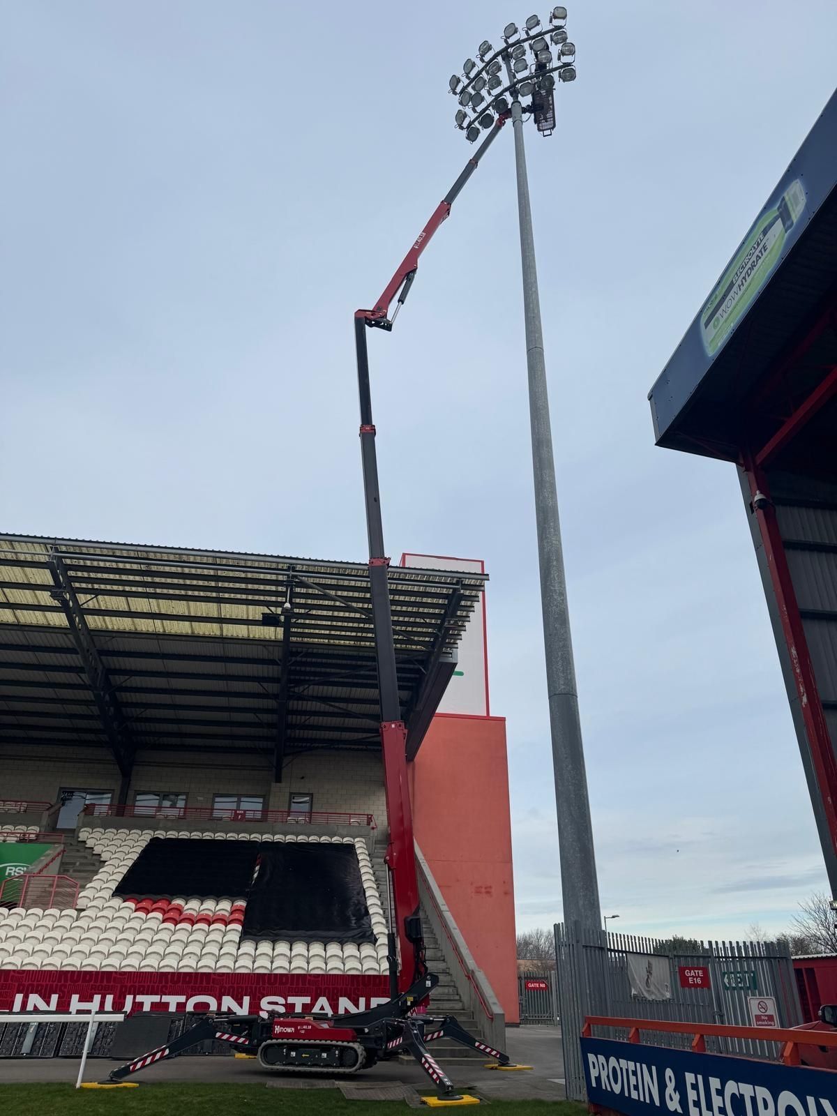 Red spider lift extended beside a stadium floodlight mast