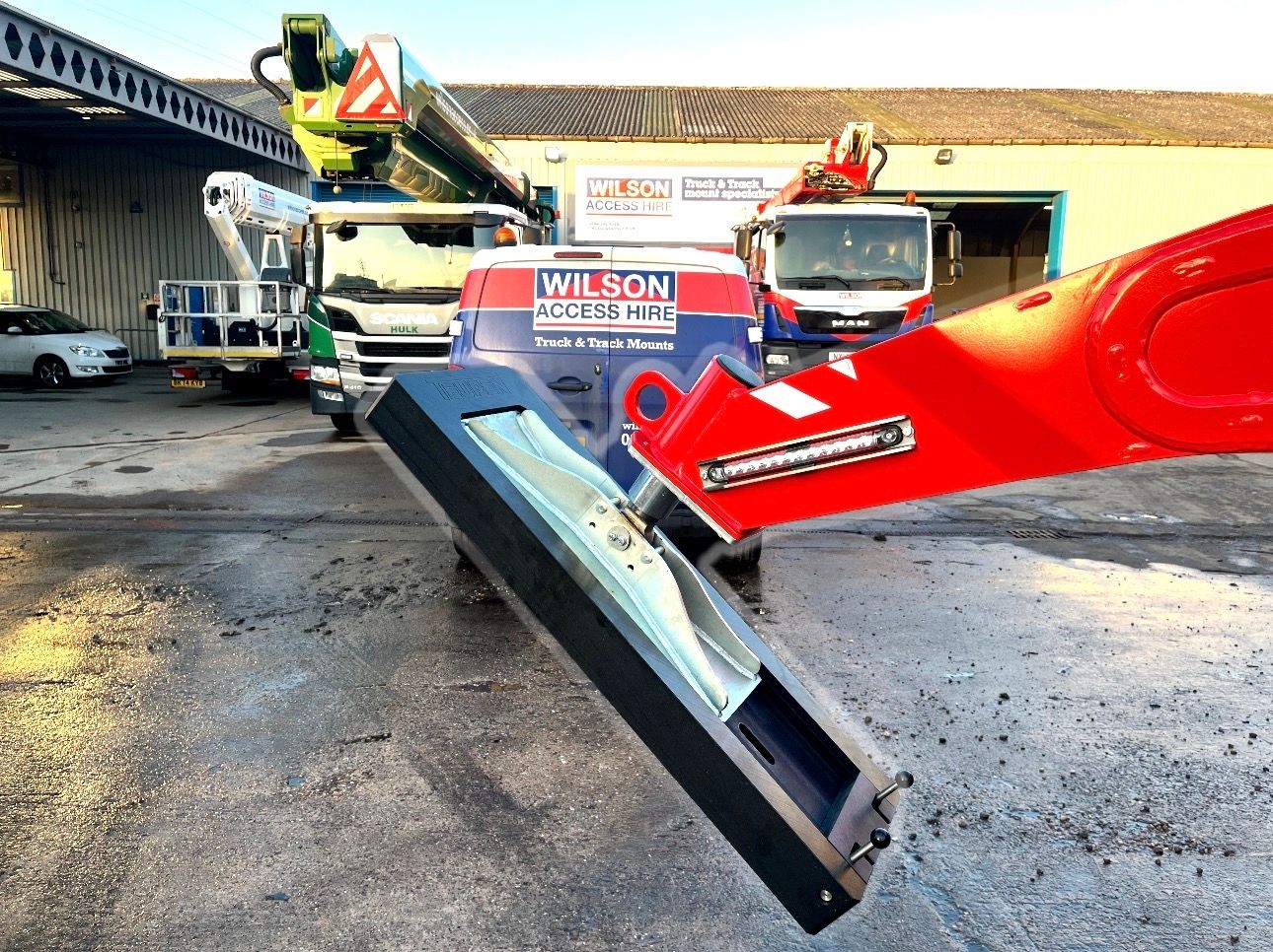 Close view of a red outrigger foot lowered onto a black spreader pad in an access-hire yard