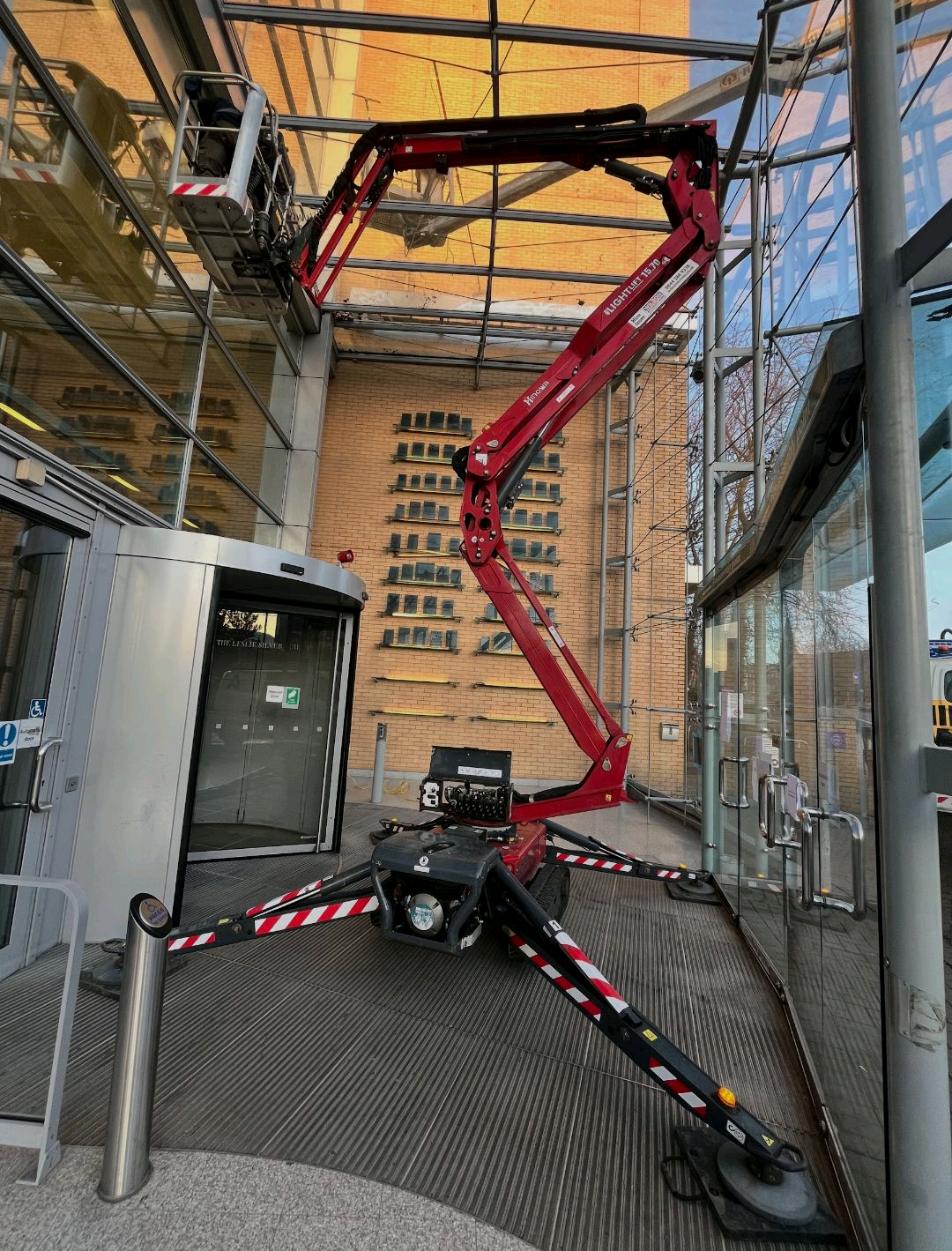 Red spider lift set on four outriggers in a narrow glazed entrance with its boom raised